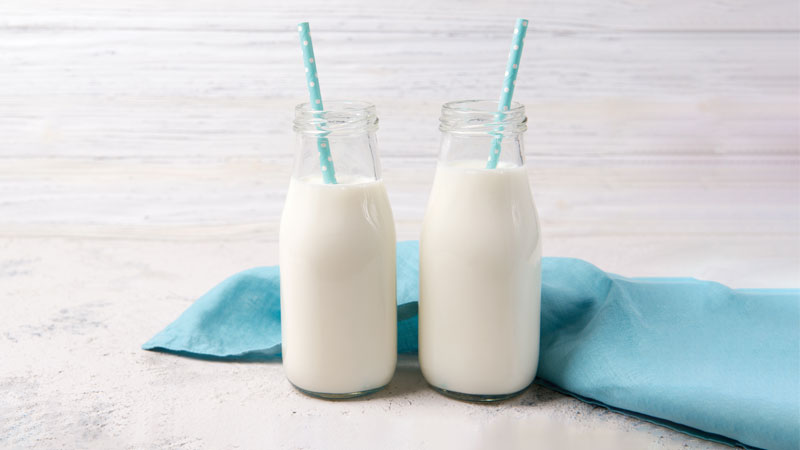 Duas garrafas pequenas de leite com uma palhinhas azuis em cada uma